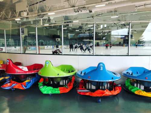 Colorful bumper cars lined up in front of an ice rink where people are playing hockey.