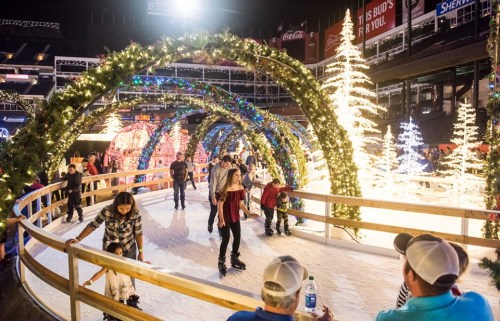 A festive ice skating rink with holiday decorations, featuring families and children skating under illuminated arches.