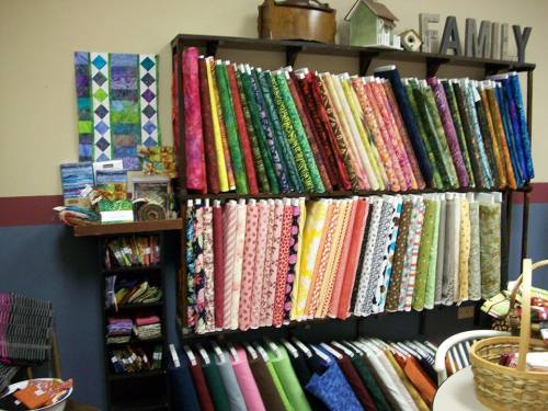 A colorful display of various fabric rolls arranged on shelves, with quilting supplies and decor in a cozy craft space.
