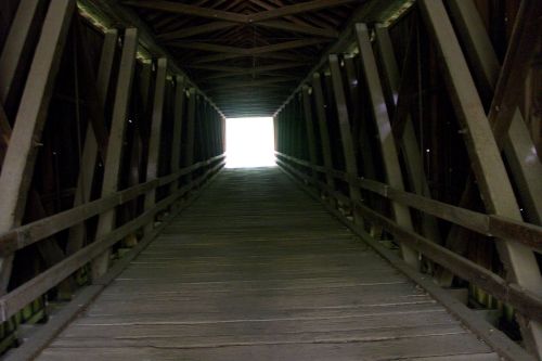 A wooden covered bridge with a long, dark tunnel leading to a bright light at the end.