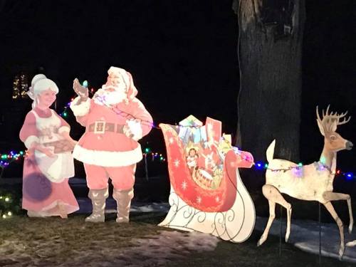 A festive scene featuring Santa, Mrs. Claus, a sleigh, and a reindeer, all decorated with colorful lights.