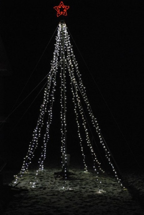 A tall, illuminated Christmas tree made of lights, topped with a red star, set against a dark night sky.