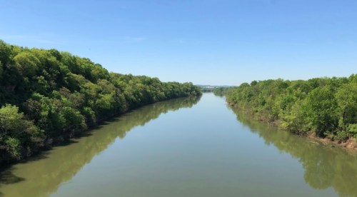 A serene river flows between lush green banks under a clear blue sky.