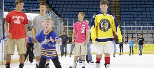 A group of young people ice skating, including a child in a blue jersey and teens in casual clothing.