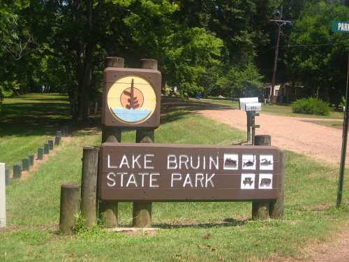 Sign for Lake Bruin State Park, featuring a boat logo and information about the park, surrounded by greenery.