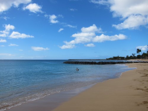 A serene beach scene with gentle waves, soft sand, and a clear blue sky dotted with clouds.