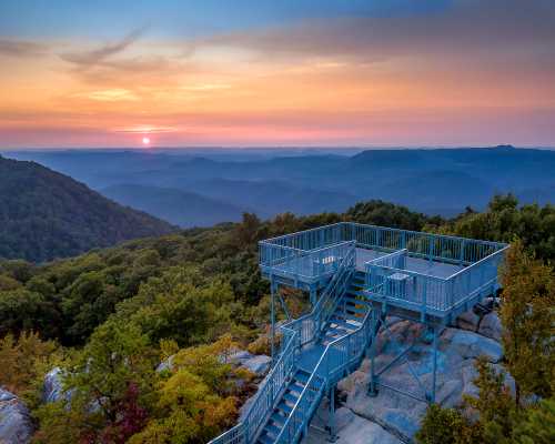 A viewing platform on a mountain at sunset, surrounded by rolling hills and a colorful sky.