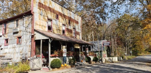 A rustic, weathered building with a sign reading "Standard Service," surrounded by autumn foliage and pumpkins.