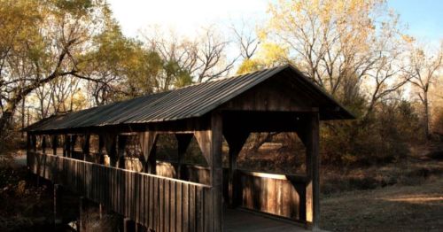 A wooden covered bridge surrounded by trees with autumn foliage under a clear sky.