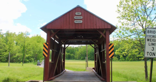 A red covered bridge with a sign reading "The Kiepps Bridge," surrounded by green fields and trees.