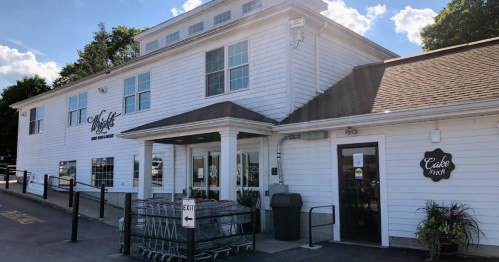 Exterior of a white building with large windows, featuring a sign for "Muff's" and a cake shop entrance.