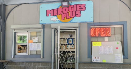 A storefront with a sign reading "Pierogies Plus" and an illuminated "OPEN" sign. Menu items are posted nearby.