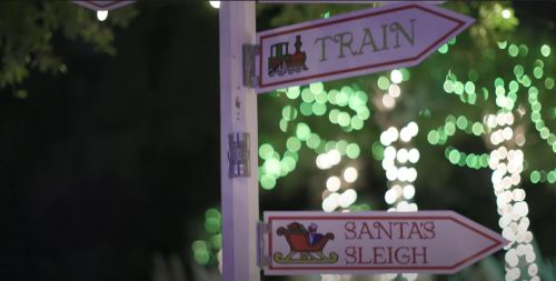 Signpost with arrows pointing to "Train" and "Santa's Sleigh," surrounded by festive lights.