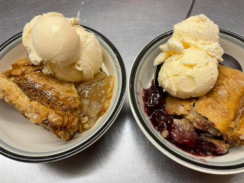 Two bowls of pie: one with apple pie and vanilla ice cream, the other with cherry pie and vanilla ice cream.