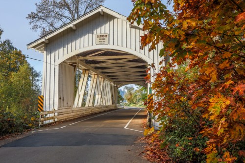 A white covered bridge with a sign, surrounded by colorful autumn foliage and a clear blue sky.