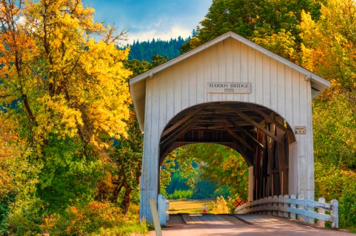 A covered bridge surrounded by vibrant autumn foliage and mountains under a clear blue sky.