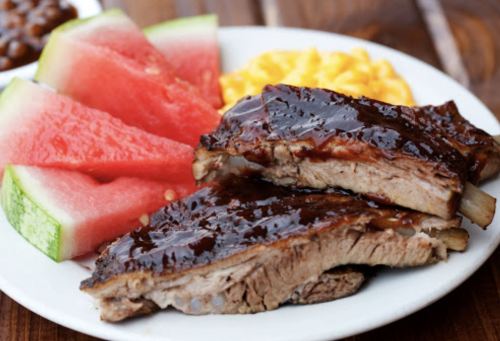 A plate with barbecue ribs, watermelon slices, and macaroni and cheese.