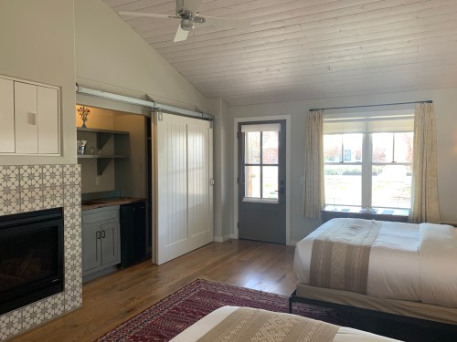 Bright, modern bedroom with two beds, a fireplace, and a sliding door leading to a small kitchenette area.