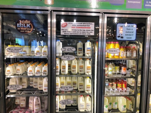 Refrigerated display case with various milk products, including coffee milk and labels indicating pasteurization and homogenization.