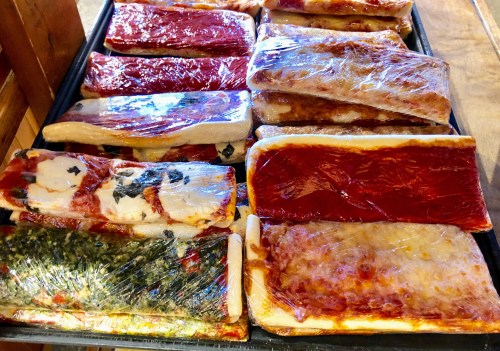A tray of various colorful, wrapped food items, including layers of sauces and toppings.