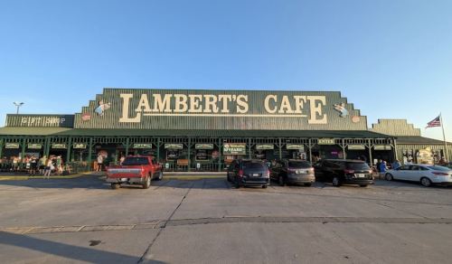 Exterior of Lambert's Cafe, featuring a green building with large signage and parked cars in front. Clear blue sky above.