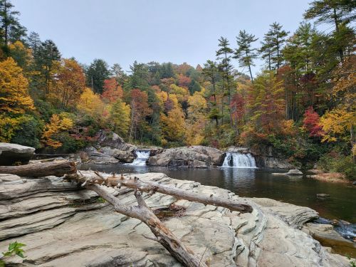 A serene river scene with waterfalls, surrounded by vibrant autumn foliage and rocky terrain.