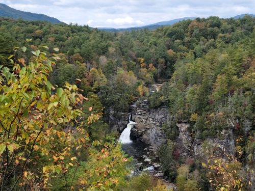 A scenic view of a waterfall surrounded by colorful autumn foliage and mountains in the background.