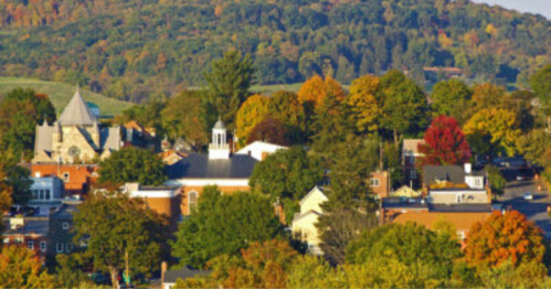 A scenic view of a small town surrounded by colorful autumn trees and rolling hills in the background.