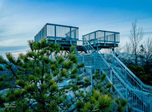 Two observation decks on a rocky hillside, surrounded by trees, under a blue sky at dusk.