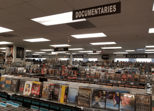 A spacious video rental store with organized shelves labeled by genre, including Action, Horror, and Documentaries.