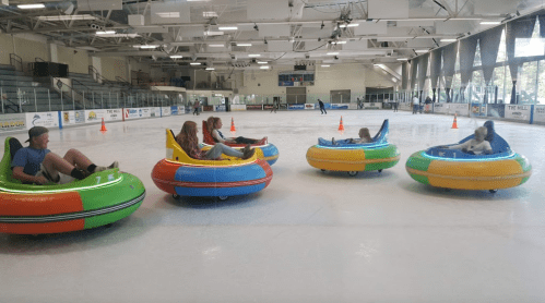 A group of people in colorful bumper cars on an ice rink, enjoying a fun activity together.