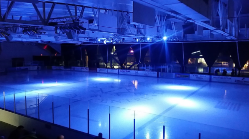 An empty ice rink illuminated by blue lights, with a darkened arena in the background.