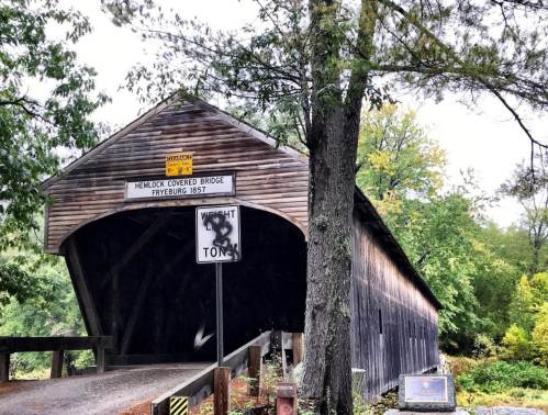 A wooden covered bridge surrounded by trees, with a sign indicating its name and year built, in a scenic setting.