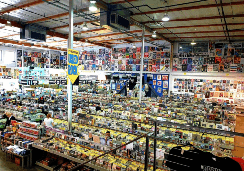 A spacious record store filled with rows of vinyl records, CDs, and colorful album covers on the walls.