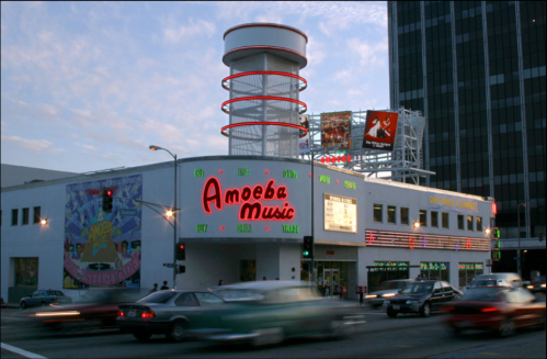 Amoeba Music storefront with neon signage, surrounded by traffic and city buildings at dusk.