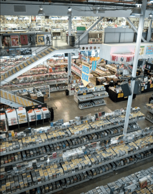 A spacious retail store filled with rows of CDs, DVDs, and posters, featuring multiple levels and bright signage.