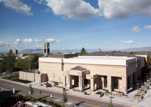 A modern building with a stone facade, columns, and a clock tower, set against a backdrop of blue skies and mountains.