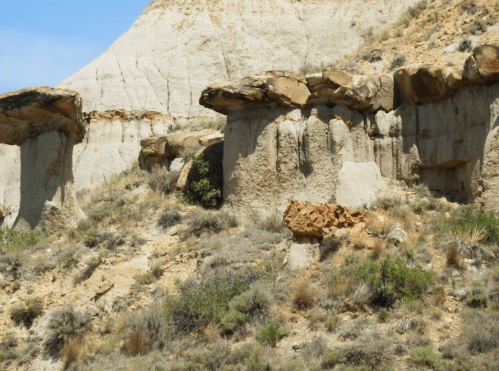 Rock formations with flat tops rise from a dry, grassy landscape under a clear blue sky.