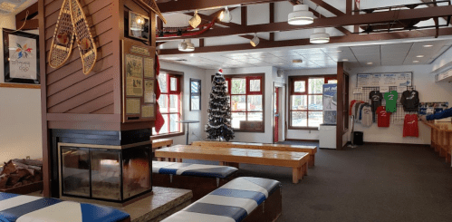 Cozy indoor space with a fireplace, wooden benches, a Christmas tree, and sports gear displayed on the walls.