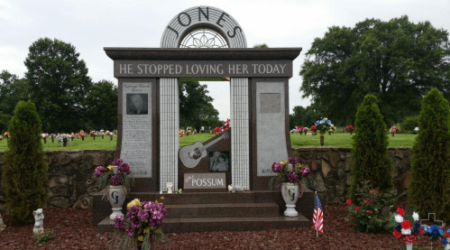 A decorative gravestone with flowers, featuring a guitar and the inscription "He stopped loving her today."
