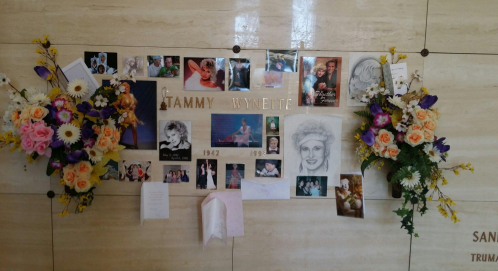A memorial display for Tammy Wynette featuring photos, flowers, and personal tributes on a wall.