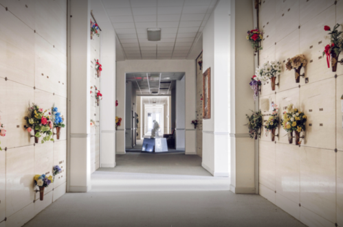 A serene hallway in a mausoleum, lined with memorials and flowers, illuminated by soft light.