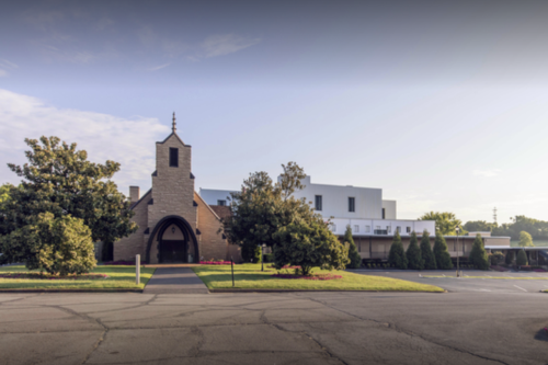 A modern church building with a stone facade and surrounding greenery, set against a clear sky.