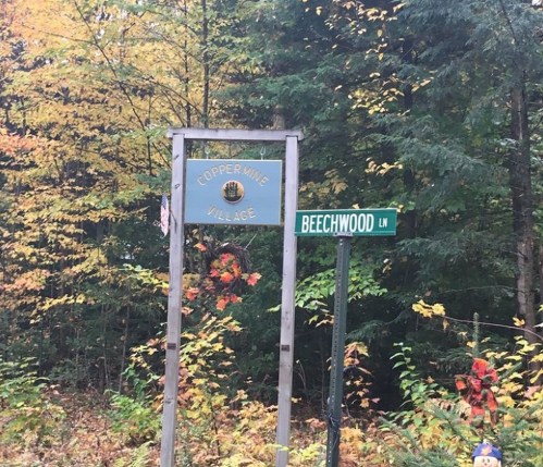 Signpost for Copper Mine Village and Beechwood Lane surrounded by autumn foliage.