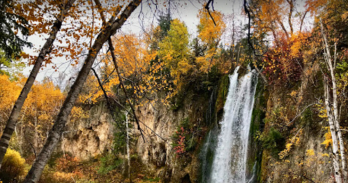 A waterfall cascades down a rocky cliff surrounded by vibrant autumn foliage.