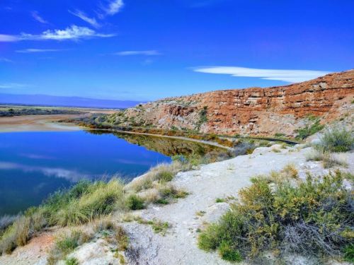 A serene landscape featuring a calm body of water, rocky cliffs, and blue skies with wispy clouds.