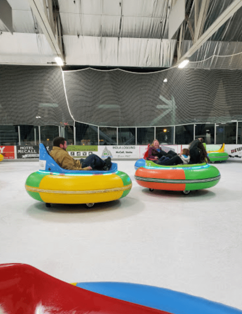 People enjoying bumper cars on ice, surrounded by a rink with colorful inflatable vehicles.