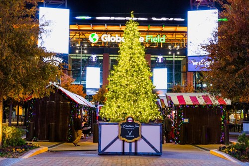 A brightly lit Christmas tree stands in front of Globe Life Field, surrounded by festive market stalls.