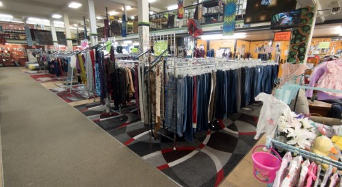 A spacious thrift store interior with racks of clothing and colorful carpets, creating a vibrant shopping atmosphere.