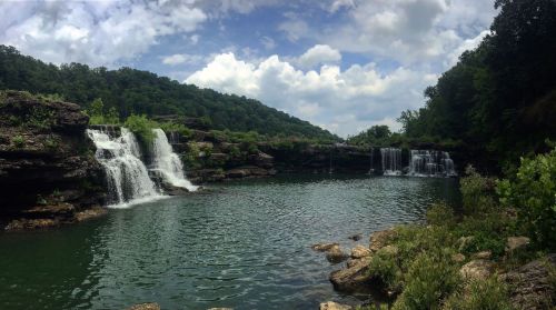 A serene landscape featuring cascading waterfalls surrounded by lush greenery and a calm, reflective pool.